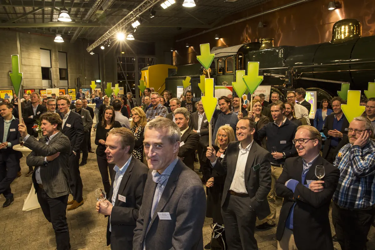 Deelnemers houden groene pijlen omhoog in een hal met een stoomlocomotief tijdens de bijeenkomst Duurzame Bedrijvigheid
