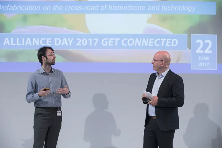 Gert-Jan Jansen en een spreker op het podium voor het scherm van Alliance Day 2017 Get Connected
