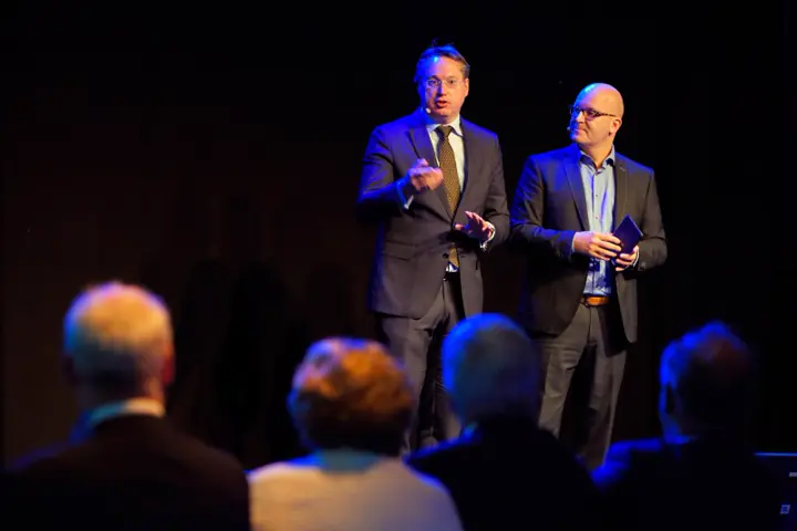 Gert-Jan Jansen en een gast op een podium in blauw licht