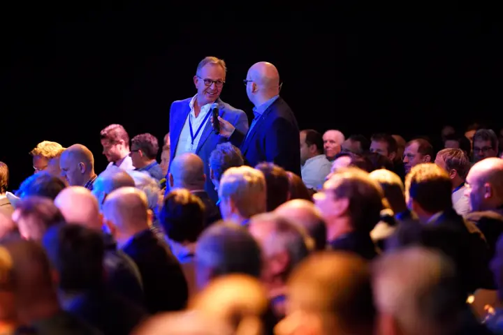 Gert-Jan Jansen en een gast op het podium voor een volle zaal in blauw licht