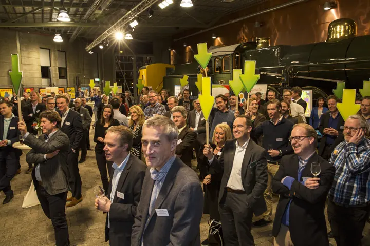 Deelnemers houden groene pijlen omhoog in een hal met een stoomlocomotief