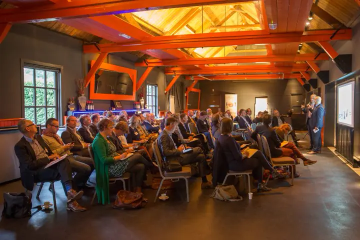 Een volle zaal onder houten spanten in oranje licht tijdens Get Connected