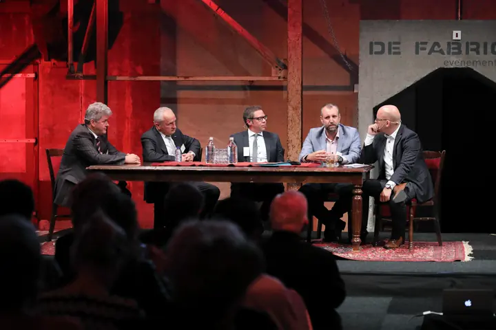Panelgesprek aan een tafel op een podium met rode verlichting