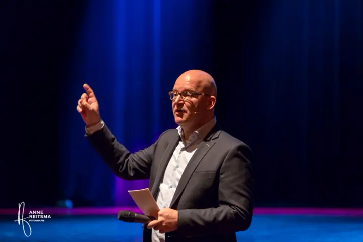 Gert-Jan Jansen wijst omhoog op een donker podium
