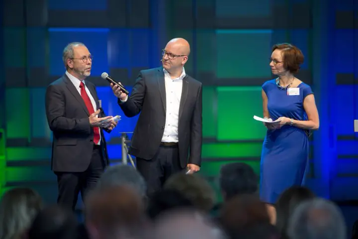 Gert-Jan Jansen met een man en een vrouw op een podium in groen en blauw licht