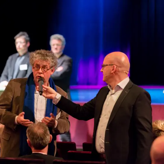 Gert-Jan Jansen houdt een gast in de zaal de microfoon voor