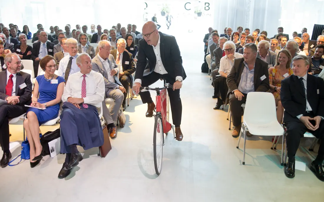 Gert-Jan Jansen fietst door het middenpad van een volle zaal tijdens de jaarvergadering van de VNCI